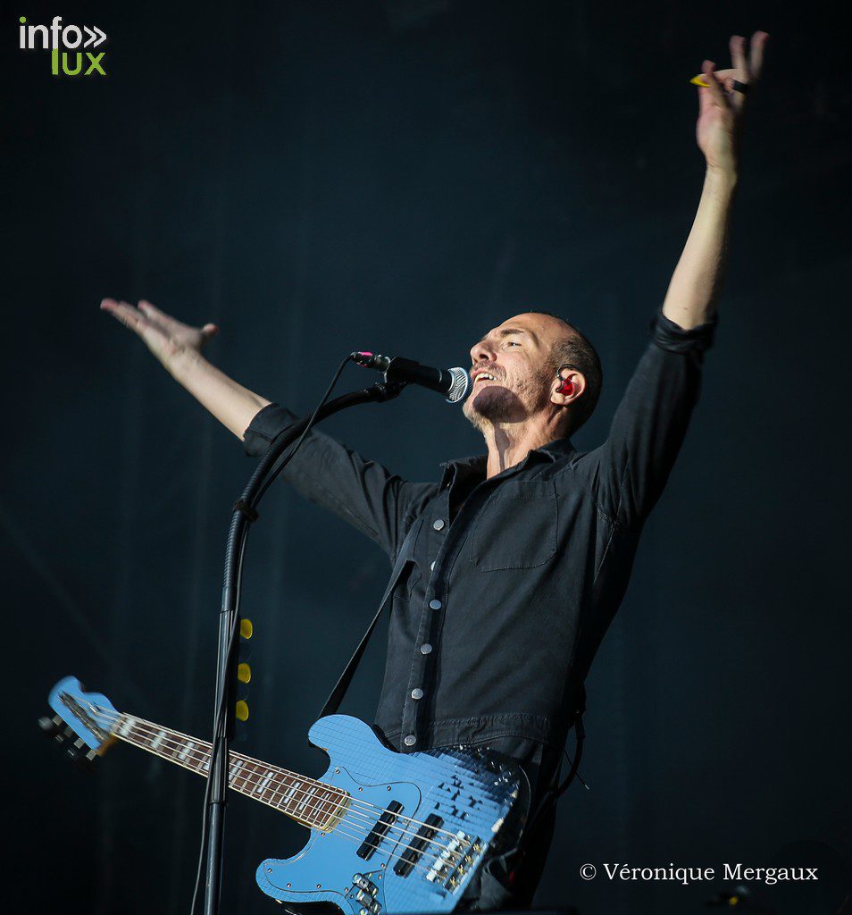 Calogero bras levés vers le public, basse bleue à la main, chemise noire