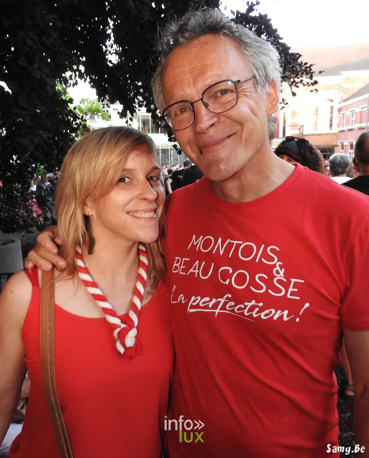 Couple au Doudou de Mons, l'homme en t-shirt rouge « Montois & beau gosse » avec un cordon rouge et blanc