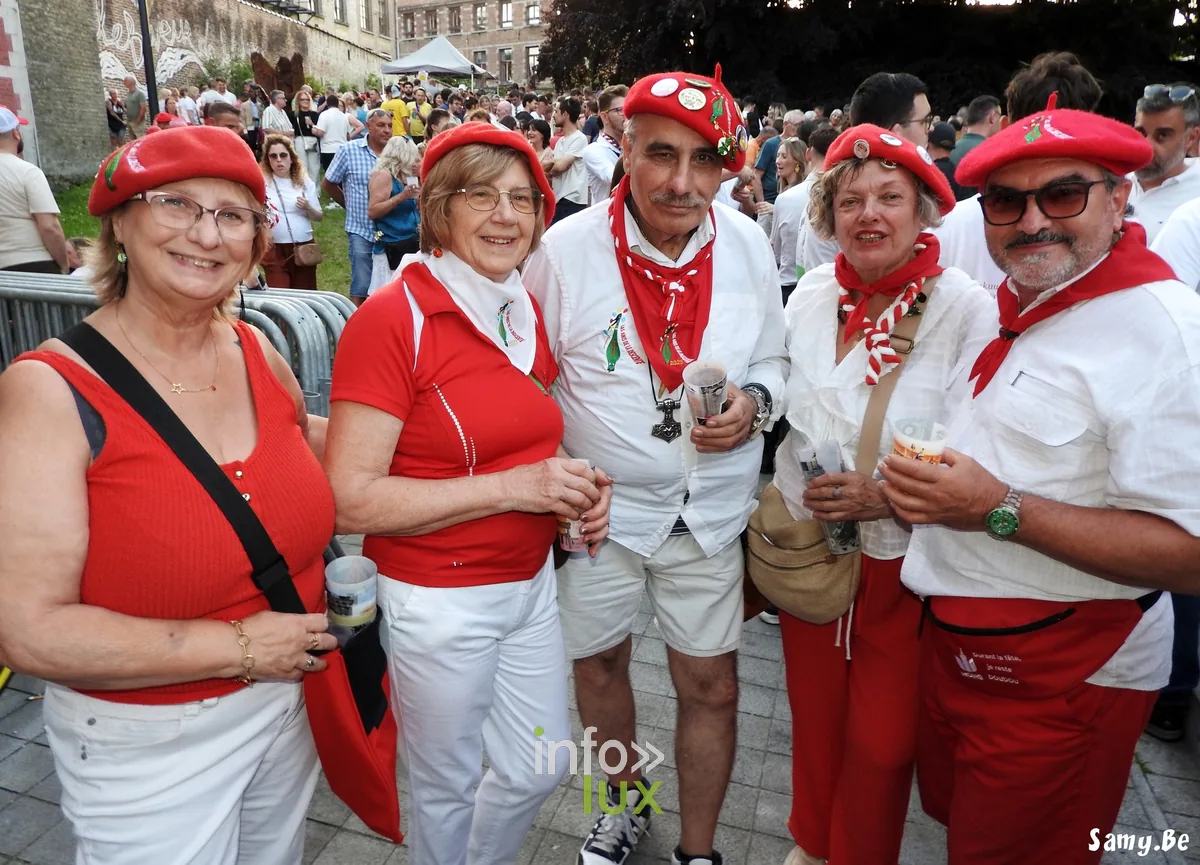 Membre d'une fanfare en polo rouge au premier plan, musiciens en rouge derrière, Doudou de Mons 2026