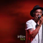 Yannick Noah chante, chapeau sur la tête, en gros plan sur fond rouge lors du concert Un p'tit tour à deux à Metz, 22 mai 2026