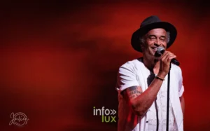 Yannick Noah chante, chapeau sur la tête, en gros plan sur fond rouge lors du concert Un p'tit tour à deux à Metz, 22 mai 2026