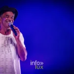 Portrait de Yannick Noah souriant au micro sous une lumière bleue, concert de Metz du 22 mai 2026