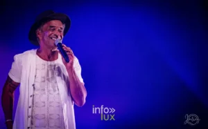 Portrait de Yannick Noah souriant au micro sous une lumière bleue, concert de Metz du 22 mai 2026