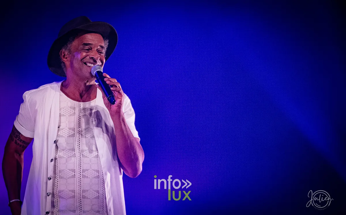 Portrait de Yannick Noah souriant au micro sous une lumière bleue, concert de Metz du 22 mai 2026