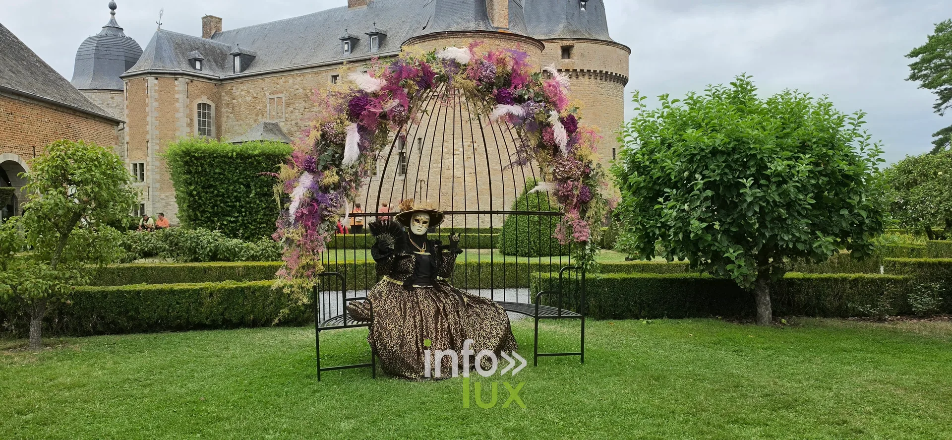 Un personnage costumé posant sous une arche fleurie dans les jardins du château