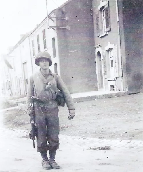 Le soldat de 1re classe Lewis Crawner dans une rue d’Ethe en septembre 1944, sa mitraillette M3 dans une main et des gaufres dans l’autre