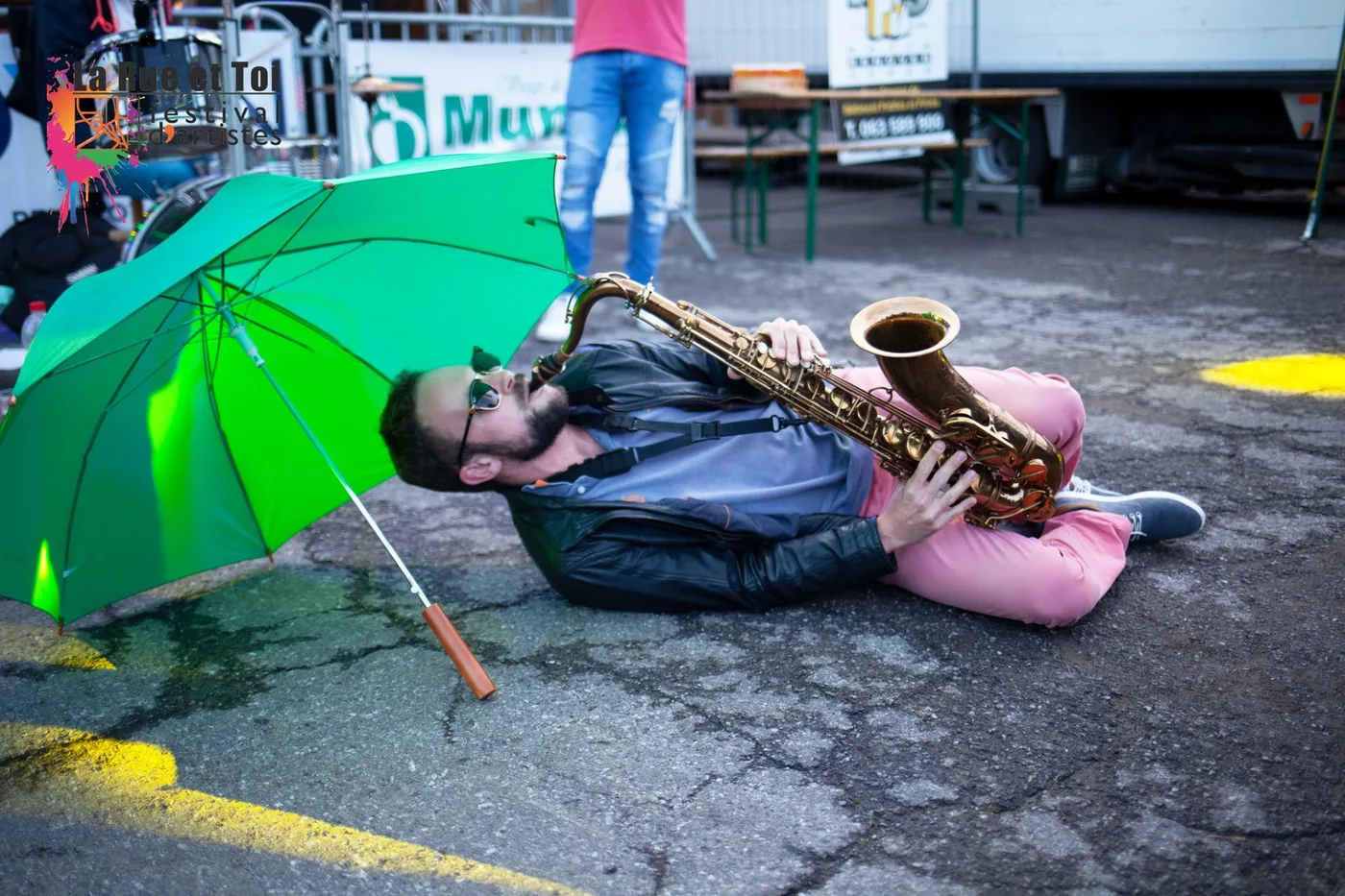 Un saxophoniste joue allonge sous un parapluie vert au festival La Rue et Toi a Ruette