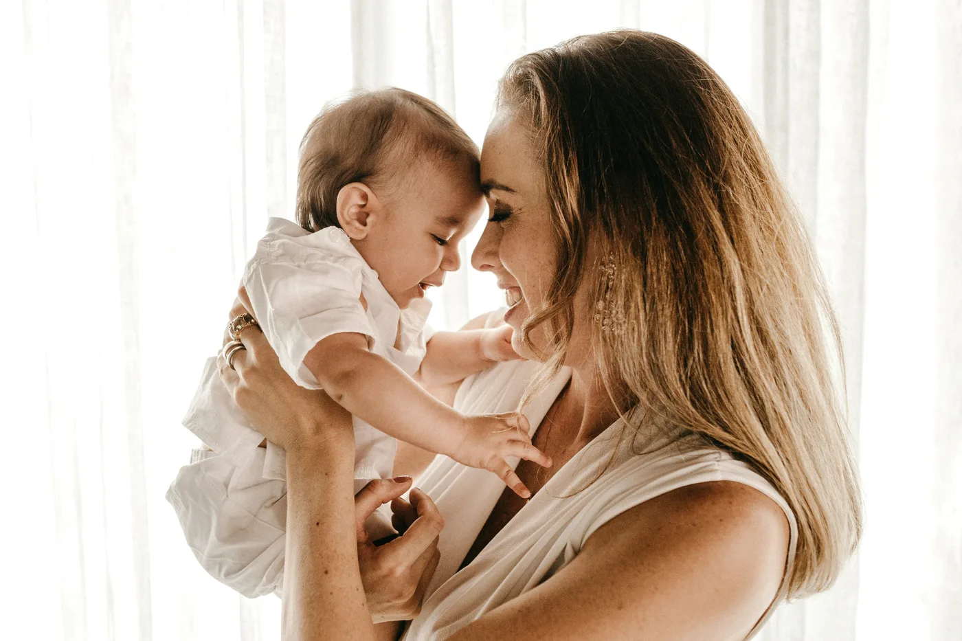 Une maman souriante tient son bébé front contre front dans une lumière douce