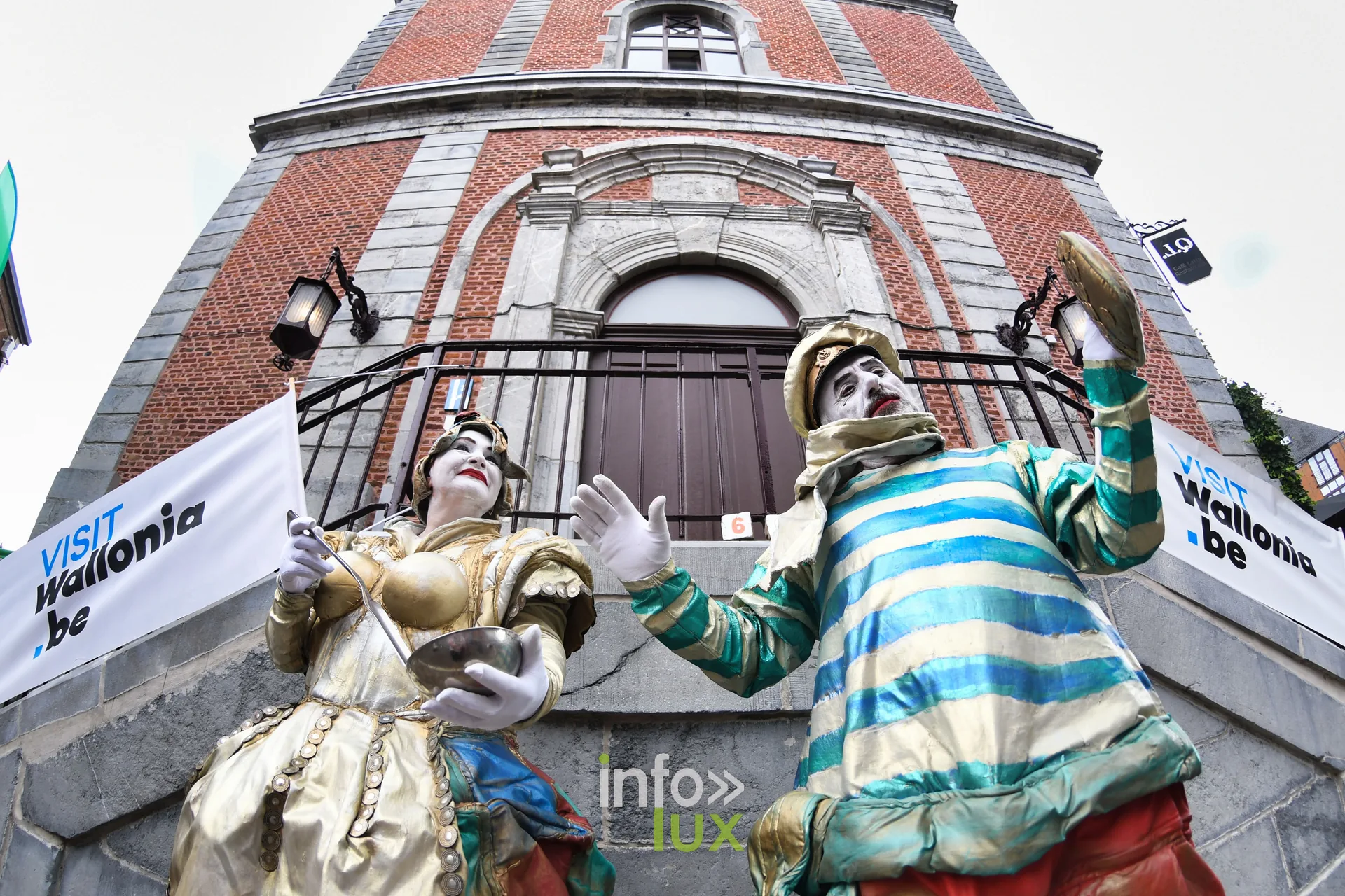 Statues vivantes costumées accrochées à une façade du centre de Marche-en-Famenne