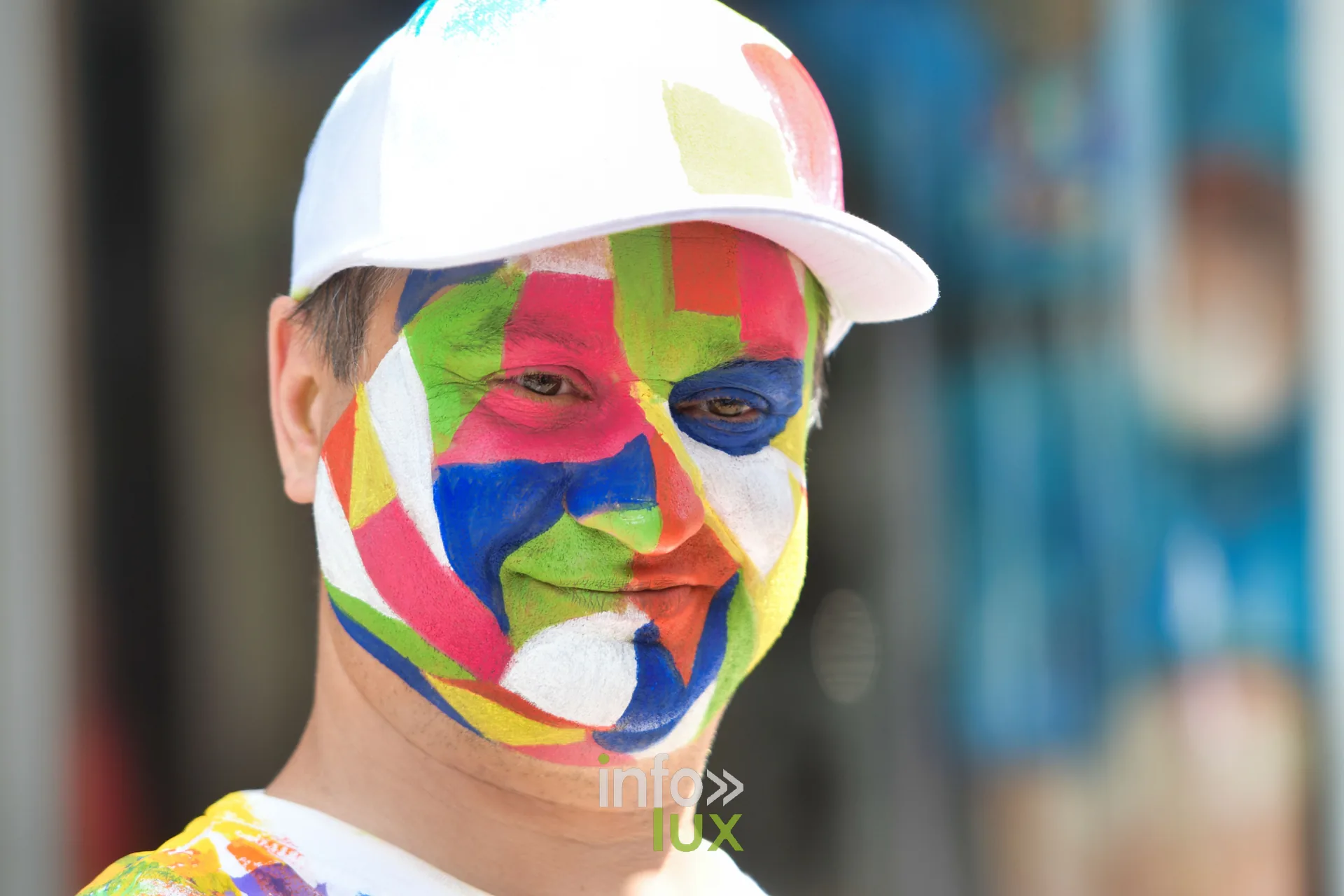 Statue vivante au visage peint multicolore et casquette blanche à Marche-en-Famenne