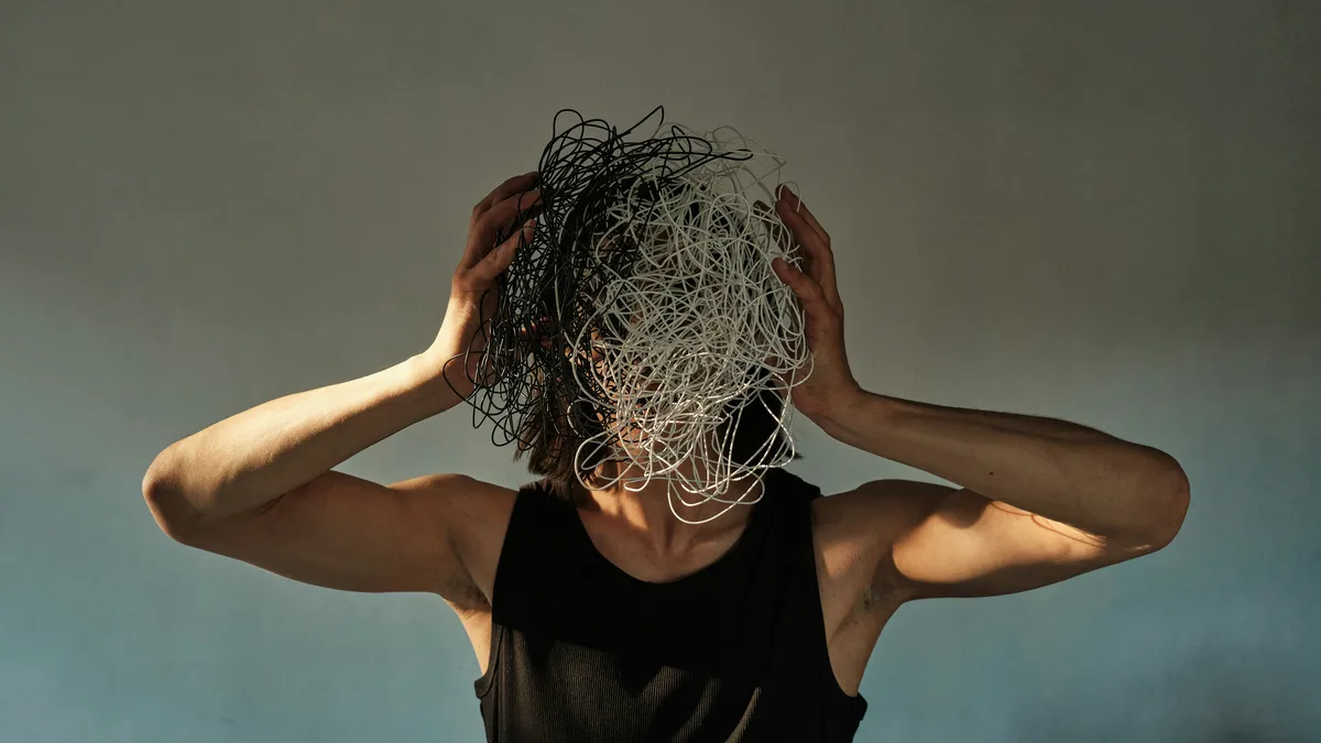 Une personne la tête entourée de fils emmêlés, image du chaos mental