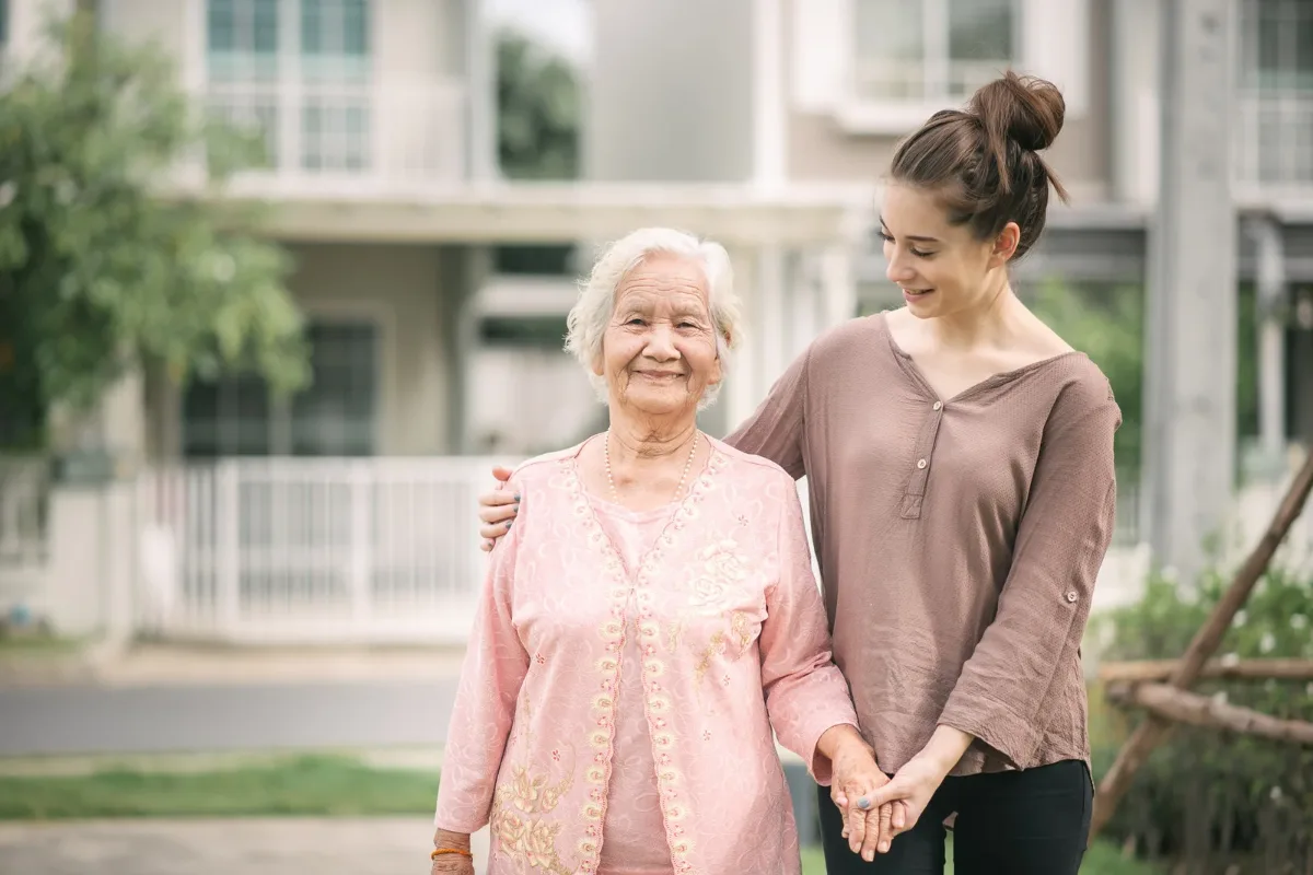 Une jeune femme accompagne une dame agee dans un jardin