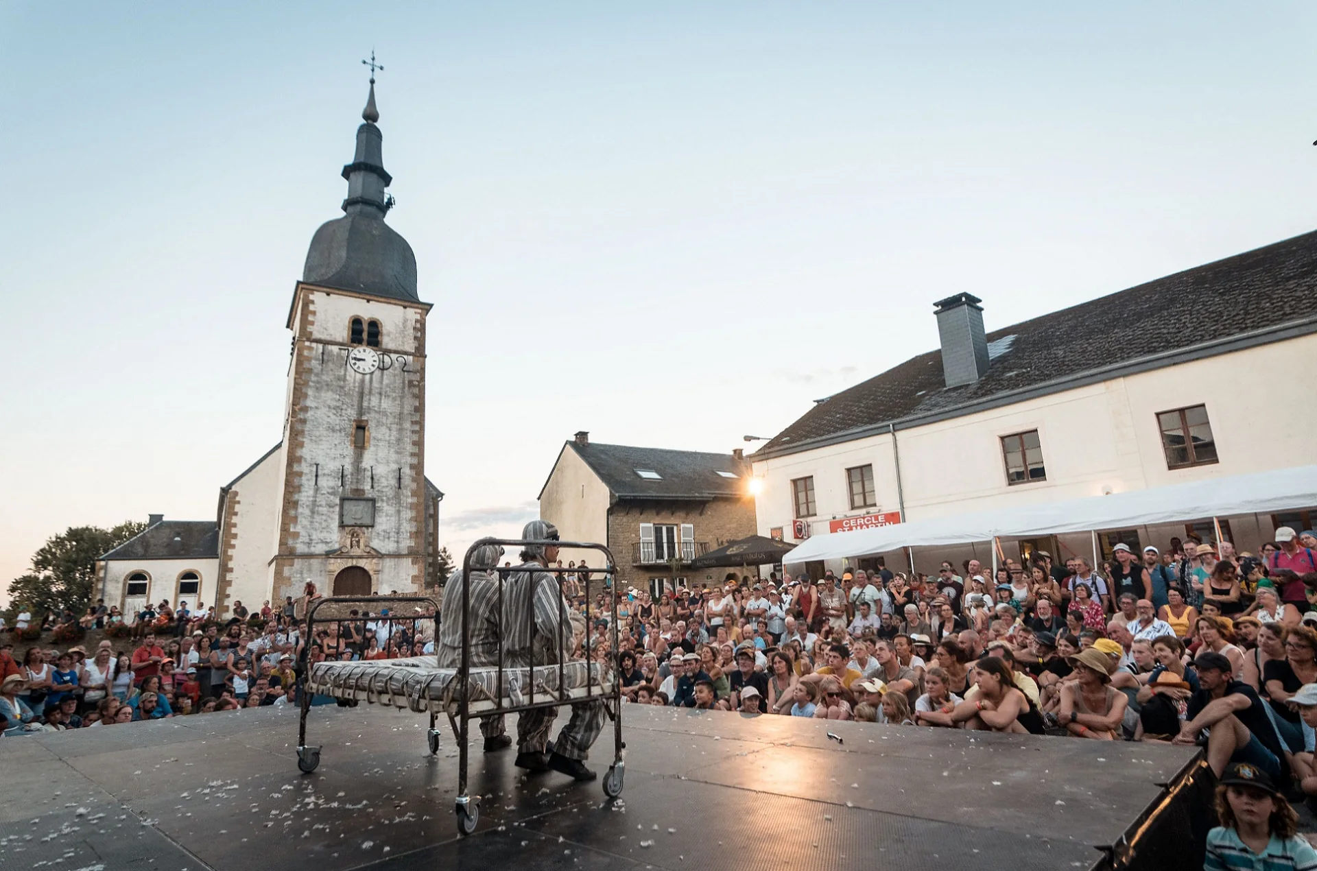 Chassepierre - spectacle sur la place du village Spectacle de rue devant l'eglise de Chassepierre, public assis en cercle sur la place du village