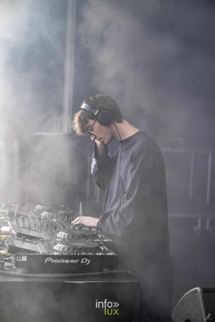 Un DJ penché sur ses platines, entouré de fumée blanche, sur la scène du festival