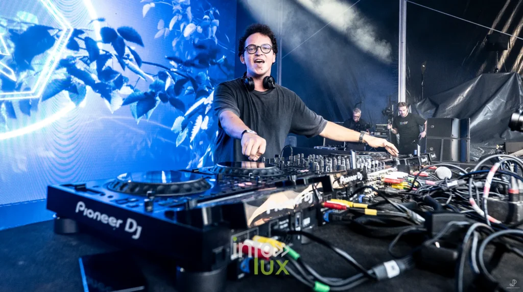 Un DJ aux platines dans une lumière bleue intense, sur la scène du festival