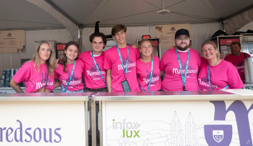 L'équipe de bénévoles en t-shirts roses Maredsous derrière le comptoir d'un bar du festival