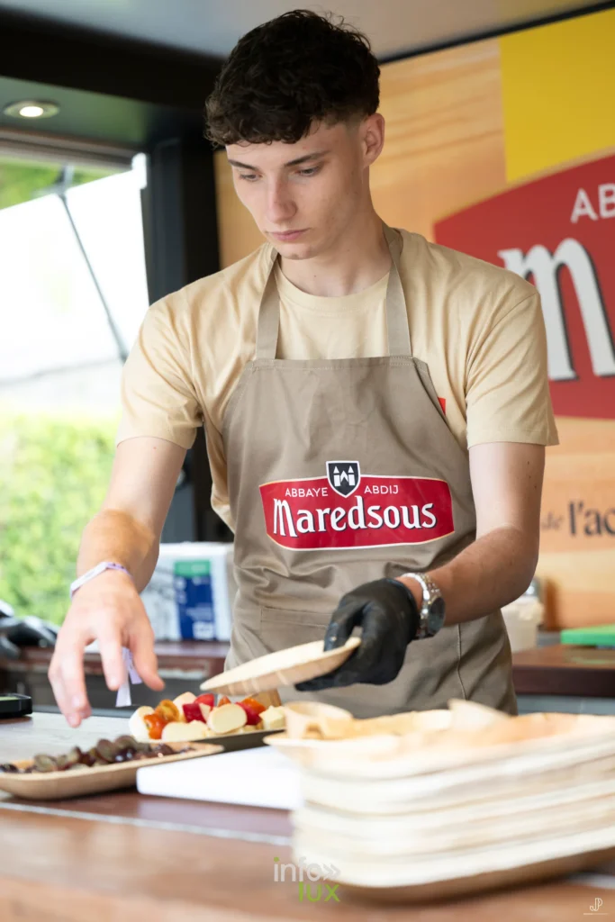 Un jeune homme en tablier Maredsous découpe une tarte au comptoir d'un stand du festival