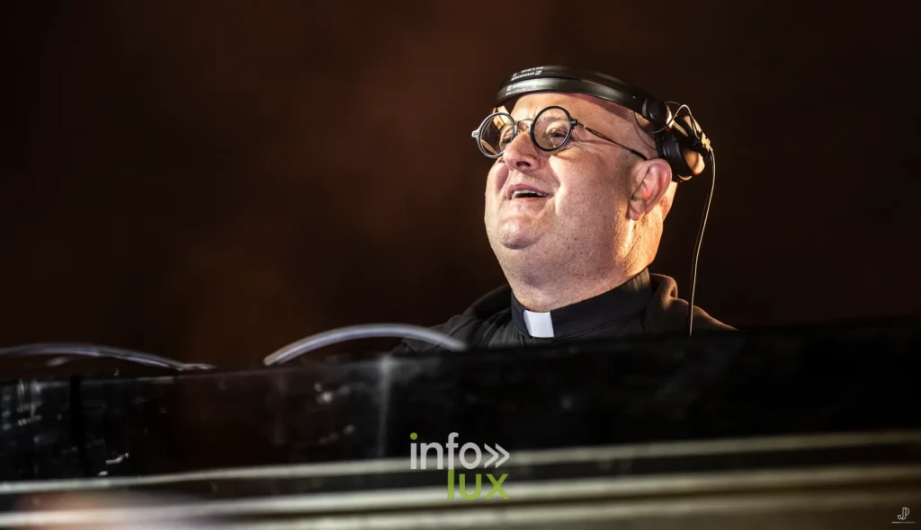 Portrait de Padre Guilherme en col romain, casque sur les oreilles, derrière sa console