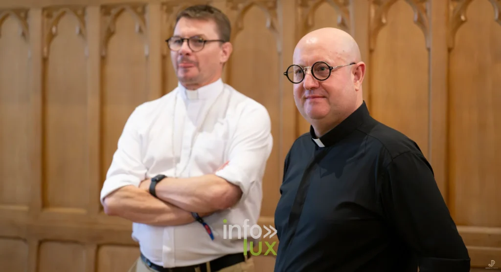 Deux religieux en col romain, souriants, sous les voûtes gothiques de l'abbaye de Maredsous