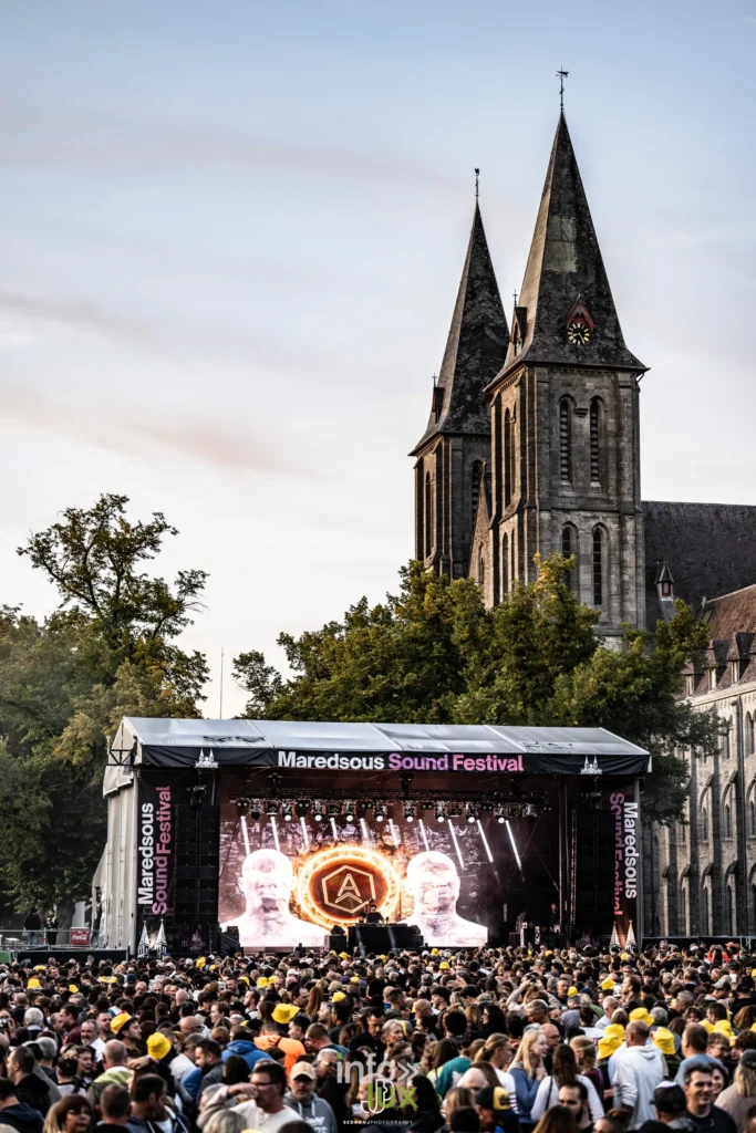 Vue large de l'abbaye de Maredsous, sa tour et la foule massée devant la scène du festival
