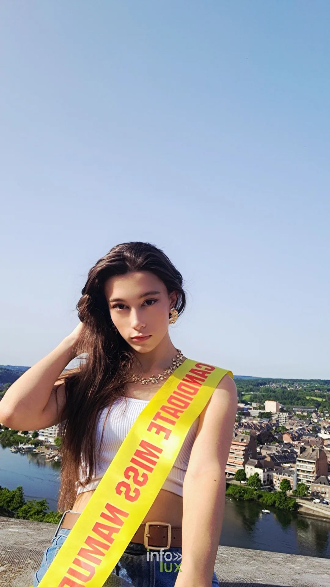 Sarahléna Manise portant l’écharpe de candidate Miss Namur, devant la vallée de la Meuse