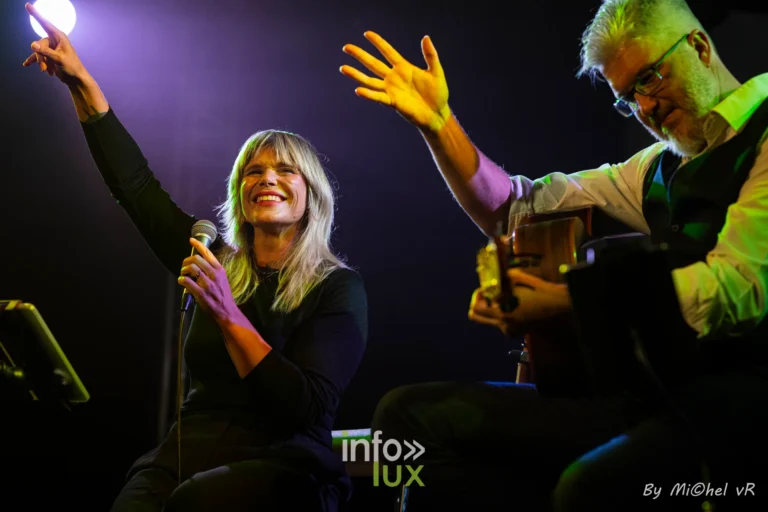 Julie Compagnon leve la main vers le public pendant qu'Antoine Goudeseune l'accompagne a la guitare, sous des projecteurs violets