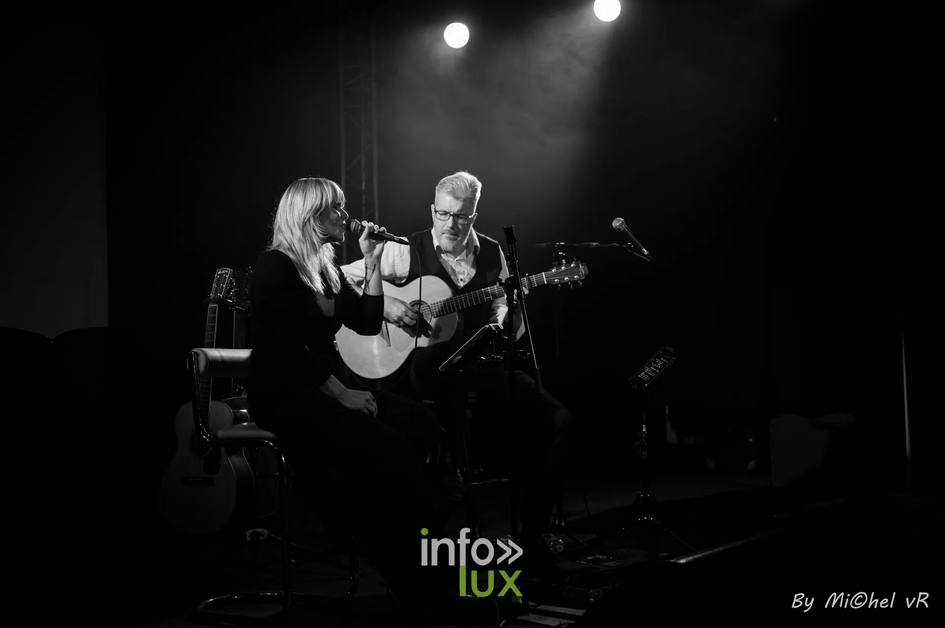 Plan large en noir et blanc de la scene du Zik-Zak avec le duo assis et ses guitares