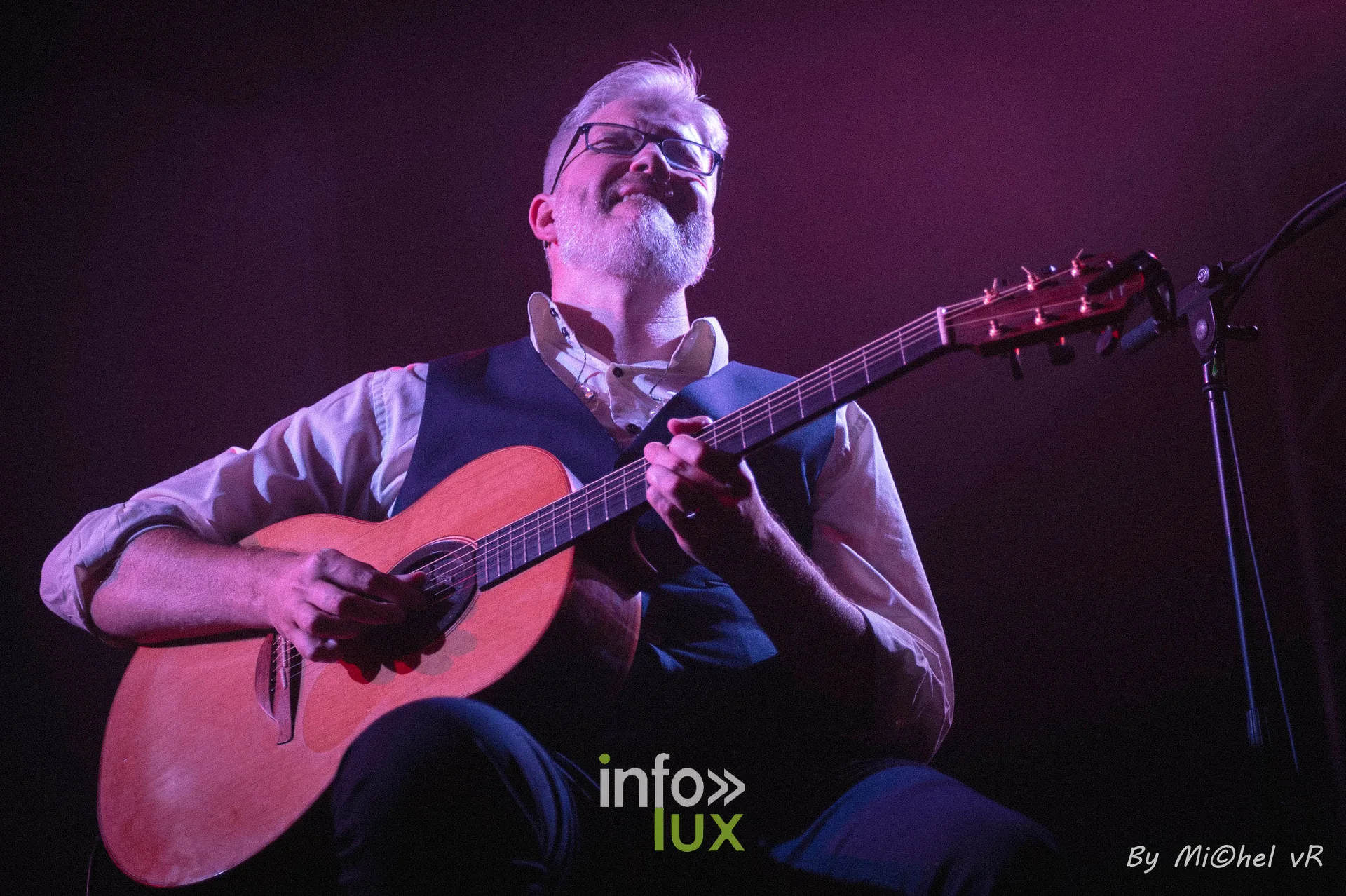 Antoine Goudeseune souriant, guitare acoustique en main, sous une lumiere rose et violette