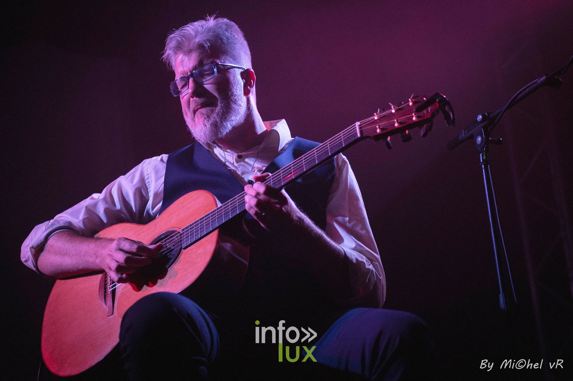 Antoine Goudeseune joue de la guitare acoustique, cadre en plan moyen, lumiere rose