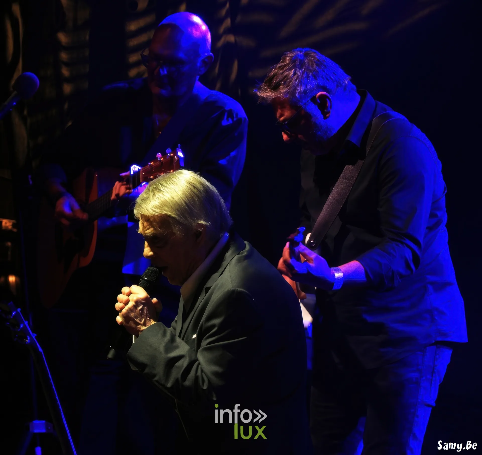 Salvatore Adamo entre deux guitaristes sous la lumière bleue – concert de Salvatore Adamo, Fêtes de Wallonie 2026, Grand-Place de Mons