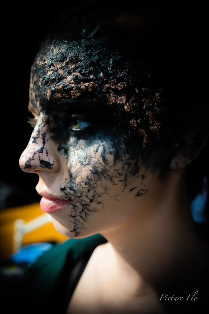 Profil d’un visage couvert de pâte noire et de feuilles bronze, coulisses de la Lux Fashion Week 2026, Arlon