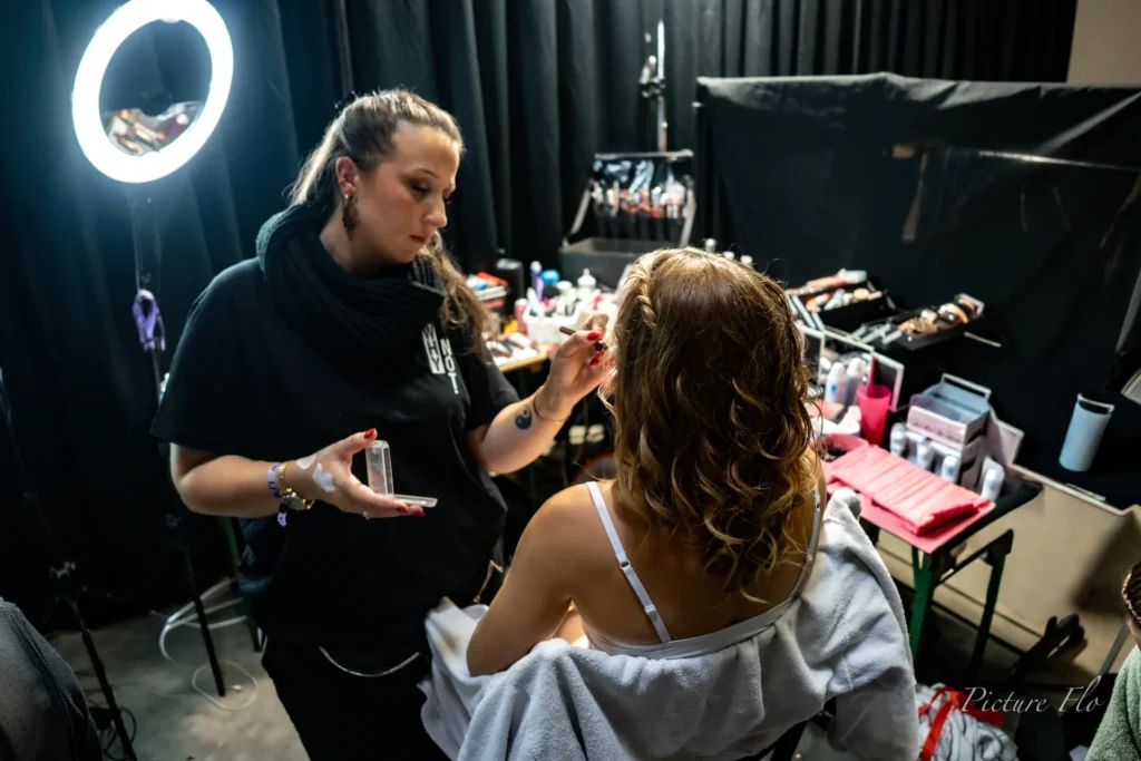 Maquilleuse au travail sous un anneau lumineux, coulisses de la Lux Fashion Week 2026, Arlon
