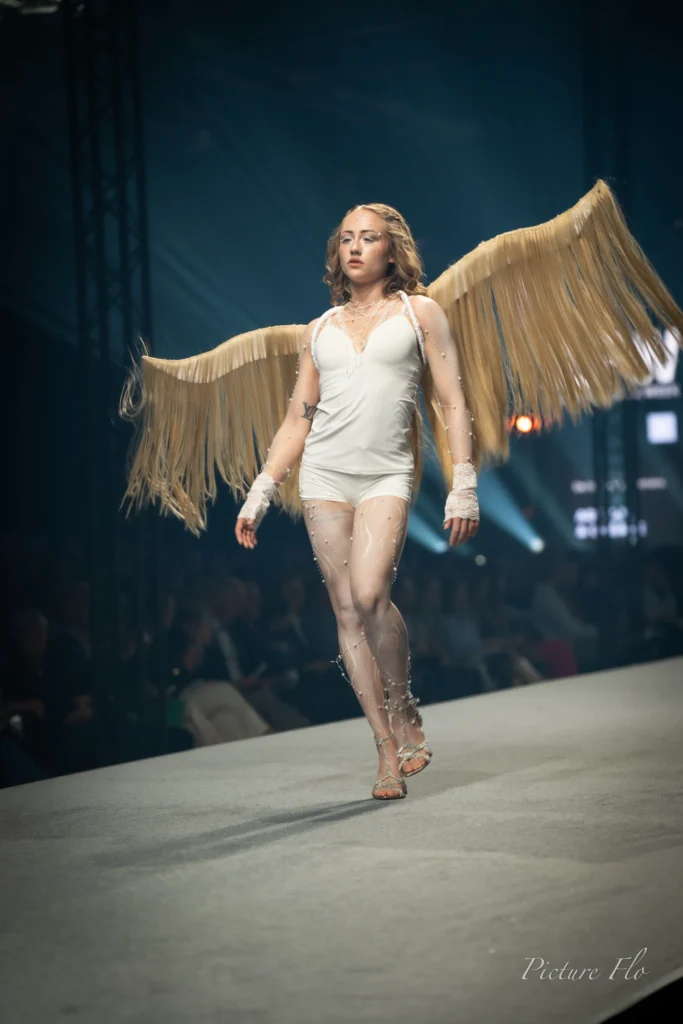 Nova, La Lumière, en body blanc avec ses ailes dorées sur le podium, Lux Fashion Week 2026, Arlon