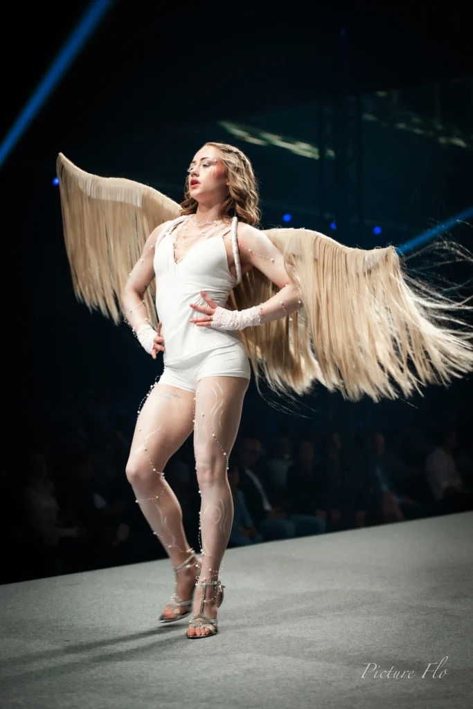 Nova en body blanc et ailes dorées, pose sur le podium, Lux Fashion Week 2026, Arlon