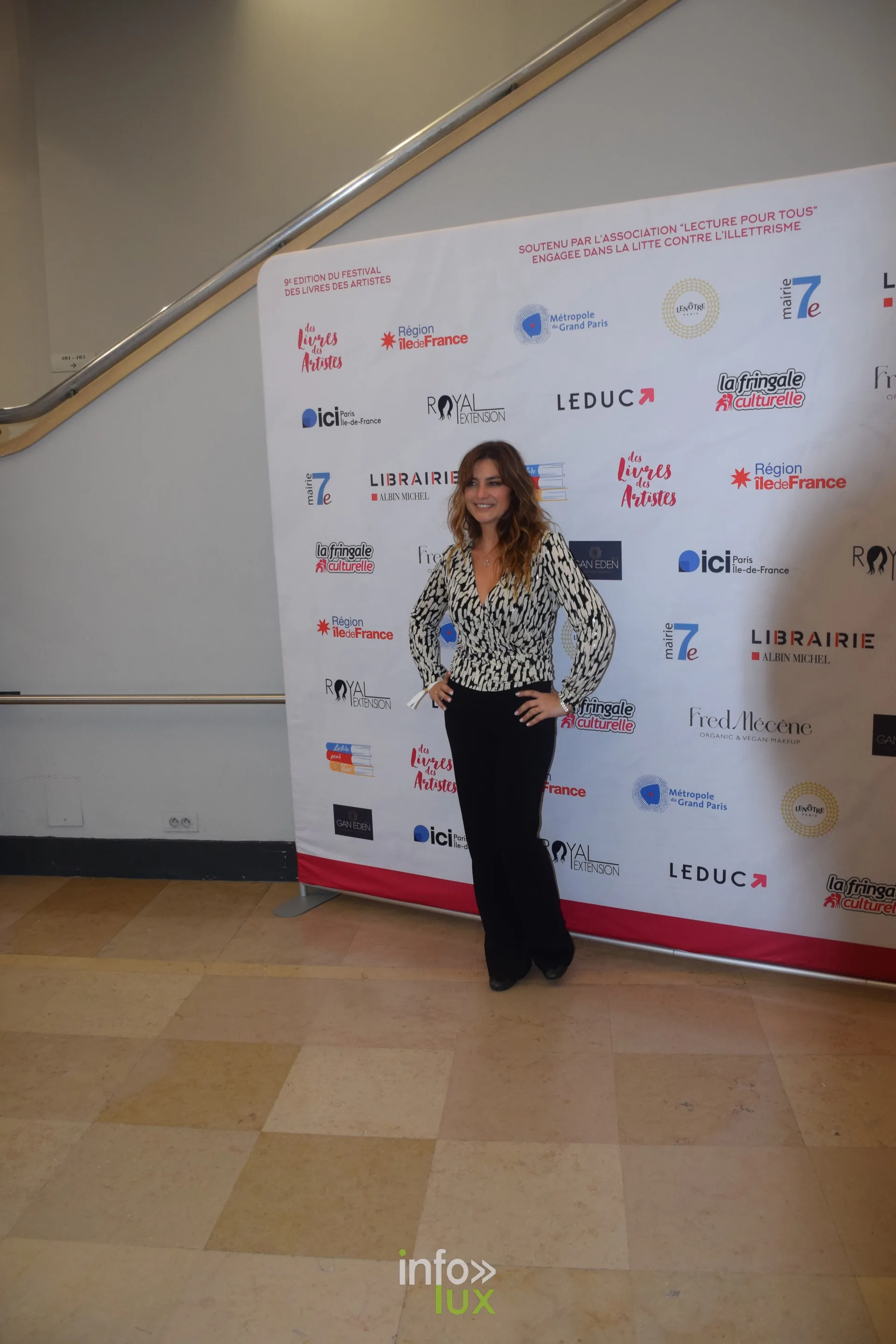 Femme posant devant un mur de logos de partenaires lors d'un salon