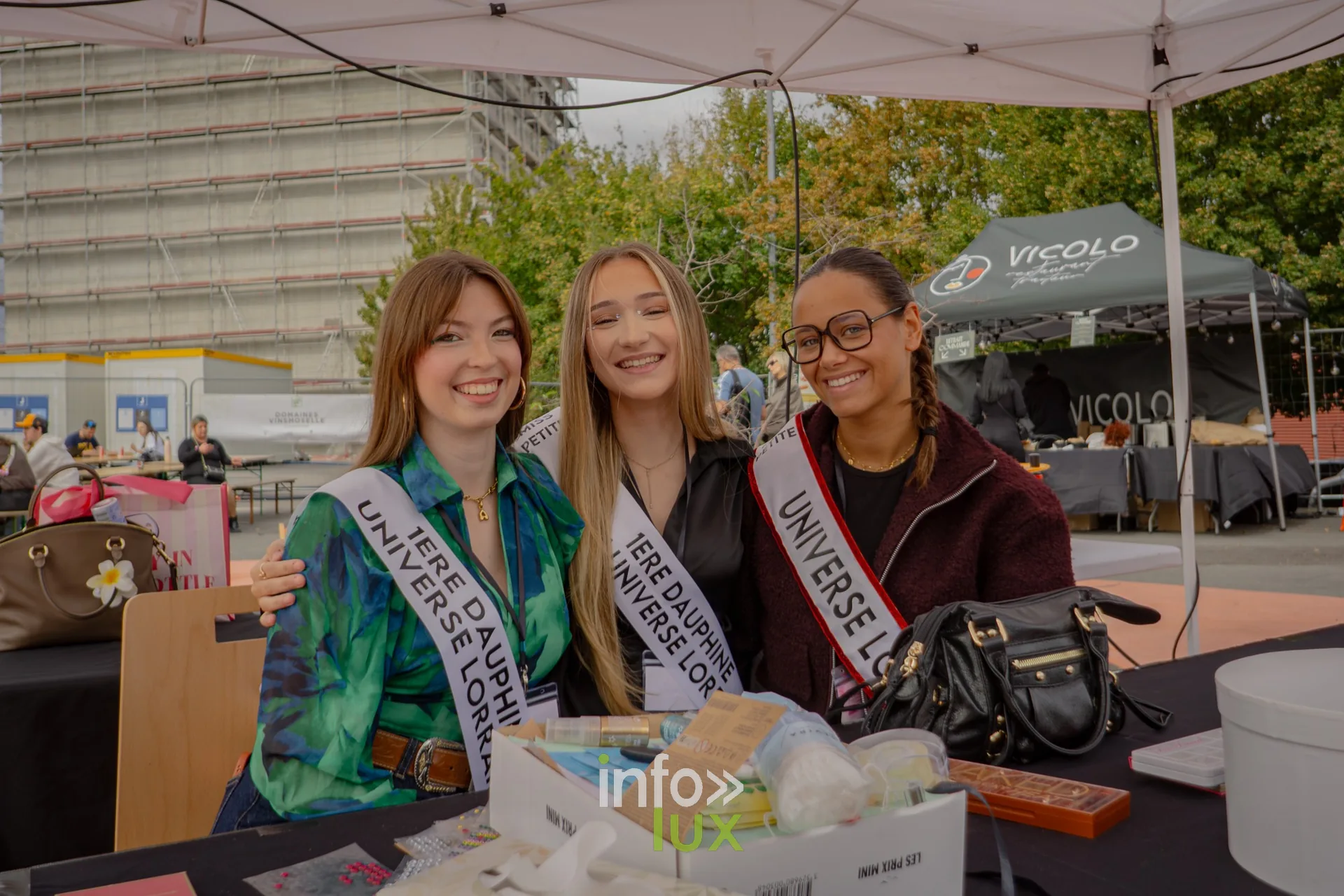 Trois jeunes femmes en écharpe de miss à un stand de l'Amné'stival