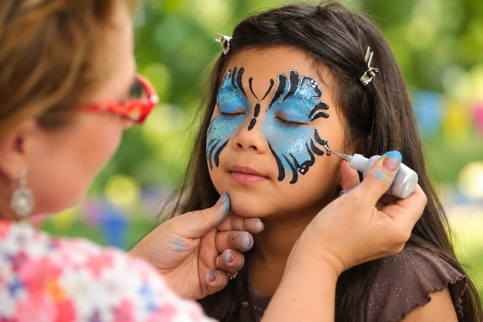 Une fillette aux yeux fermés se fait maquiller le visage en papillon bleu