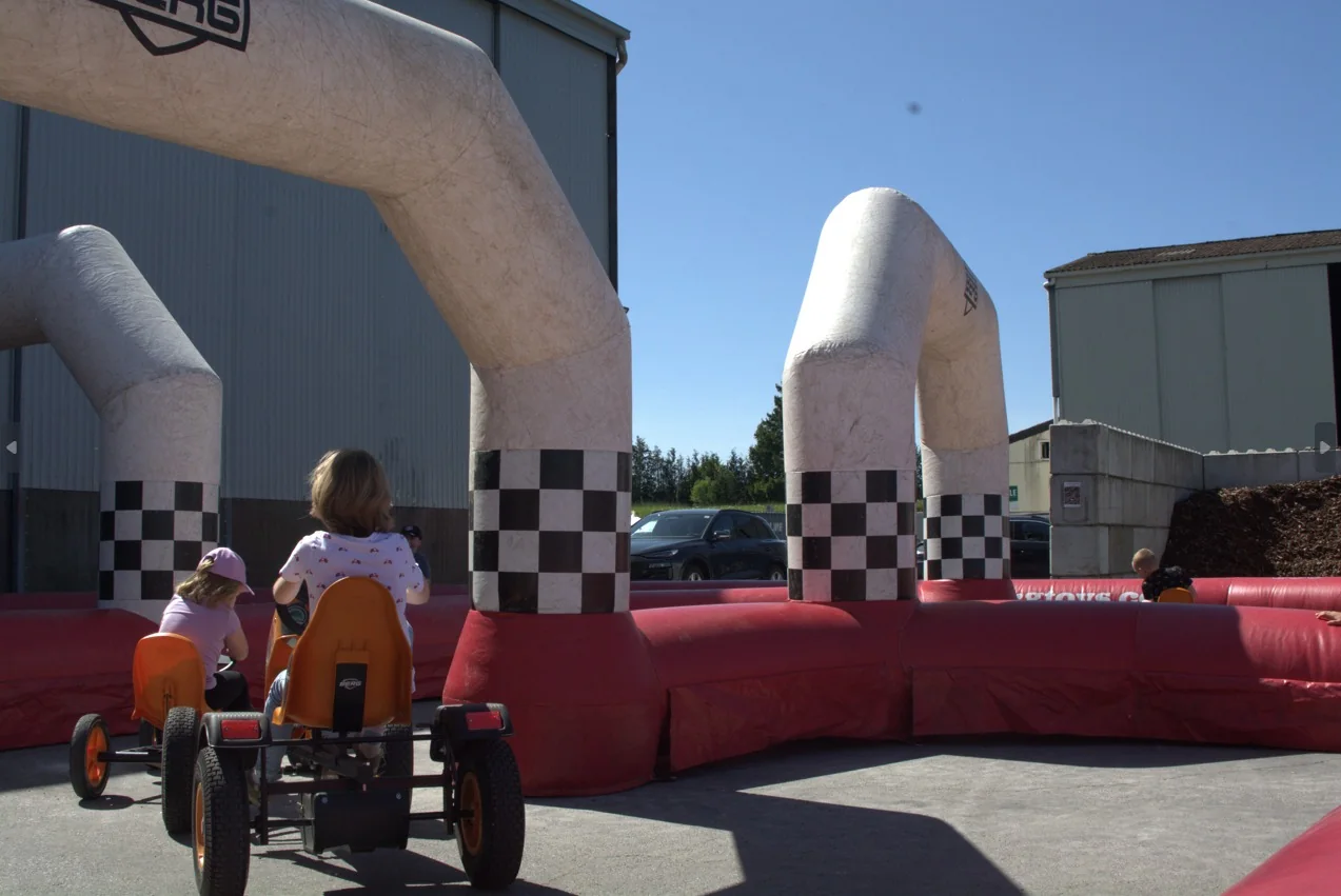 Des enfants en go-kart à pédales passent sous une arche gonflable à damier