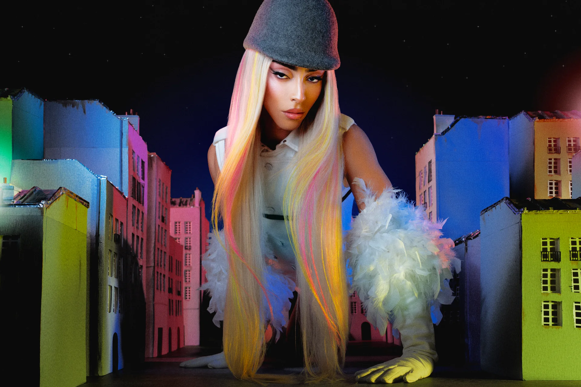 Bilal Hassani avec un boa et une casquette devant des facades parisiennes colorees