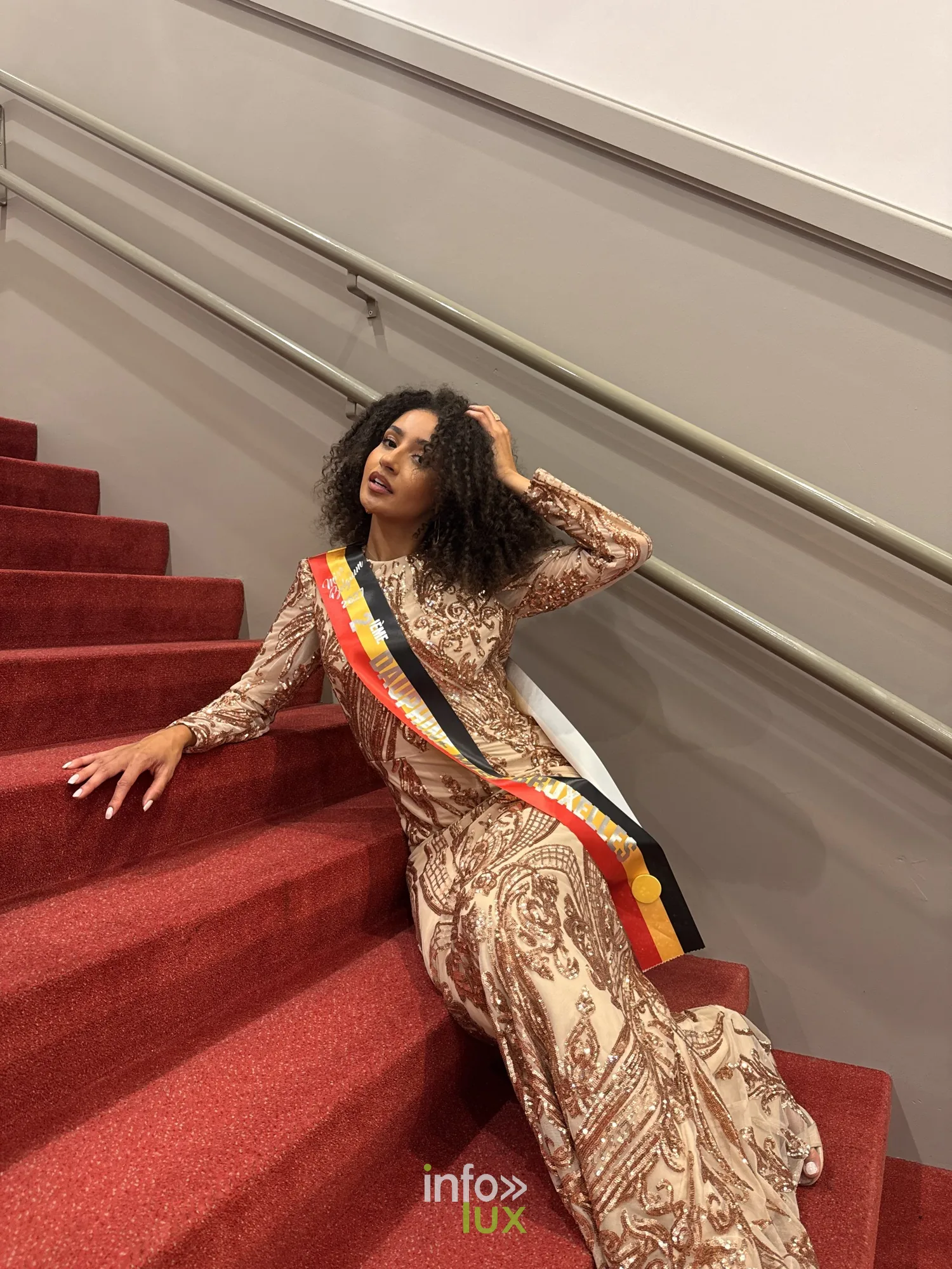 Camille en robe dorée et écharpe, assise dans un escalier au tapis rouge