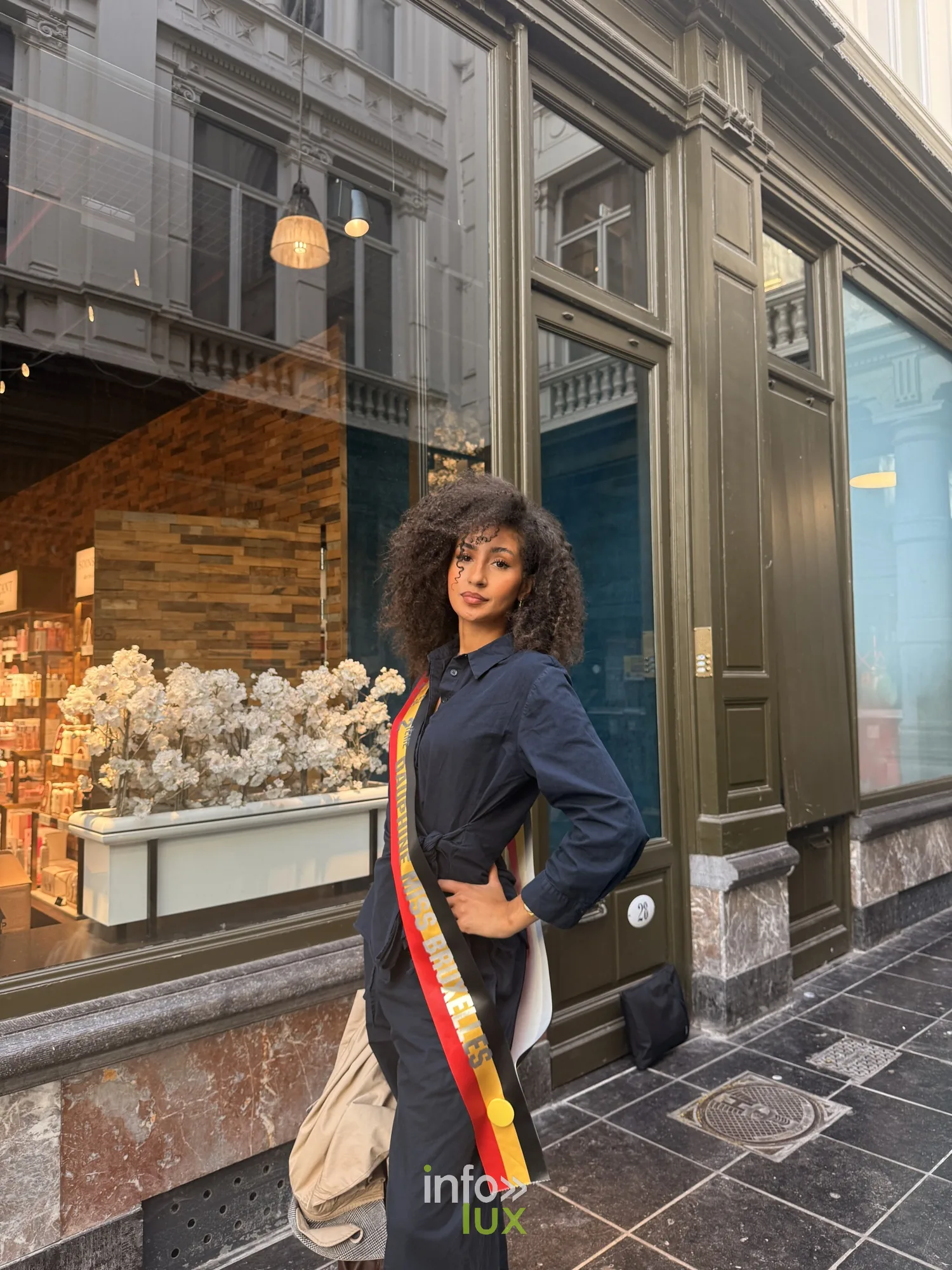 Camille en combinaison sombre avec son écharpe devant une vitrine d’une galerie à Bruxelles