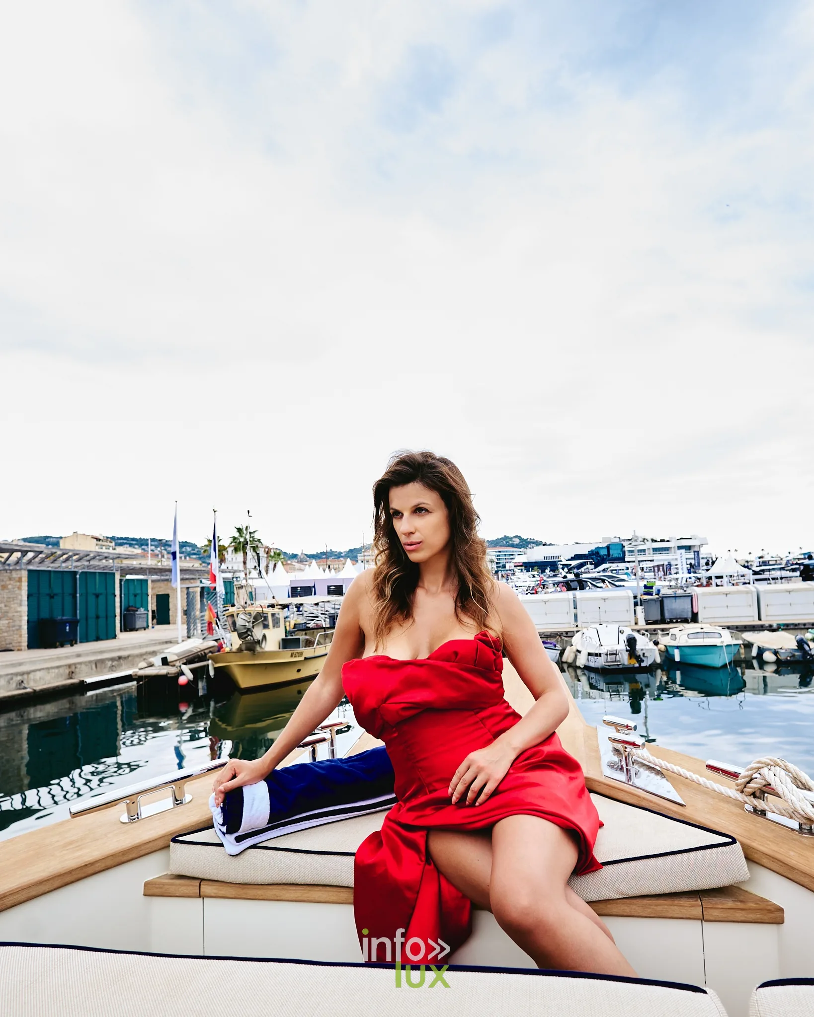 Audrey Chabotier assise à l’arrière d’un yacht en robe rouge, quai et bateaux derrière