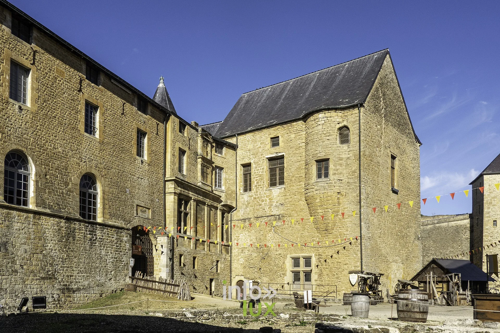 Grande cour du château fort de Sedan avec façades en pierre jaune et fanions