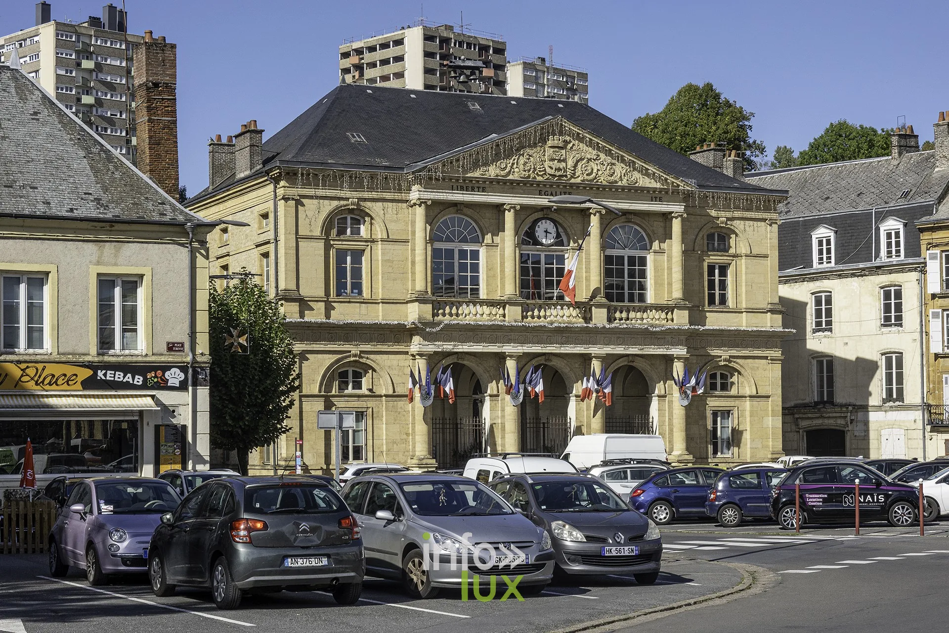 Édifice public à fronton sculpté et horloge, pavoisé de drapeaux tricolores, Sedan