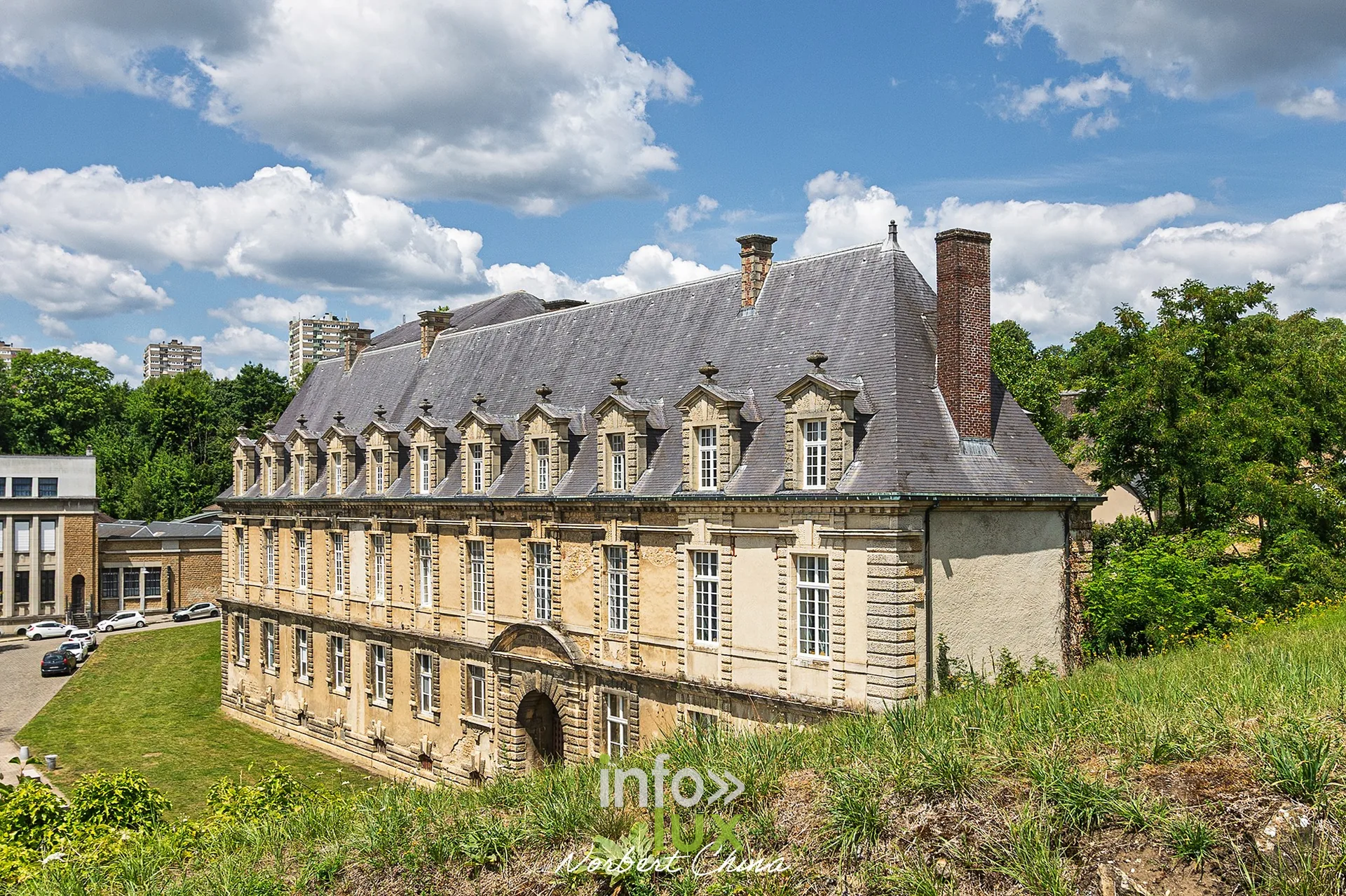 Bâtiment classique à lucarnes au pied du château fort de Sedan, pelouse au premier plan