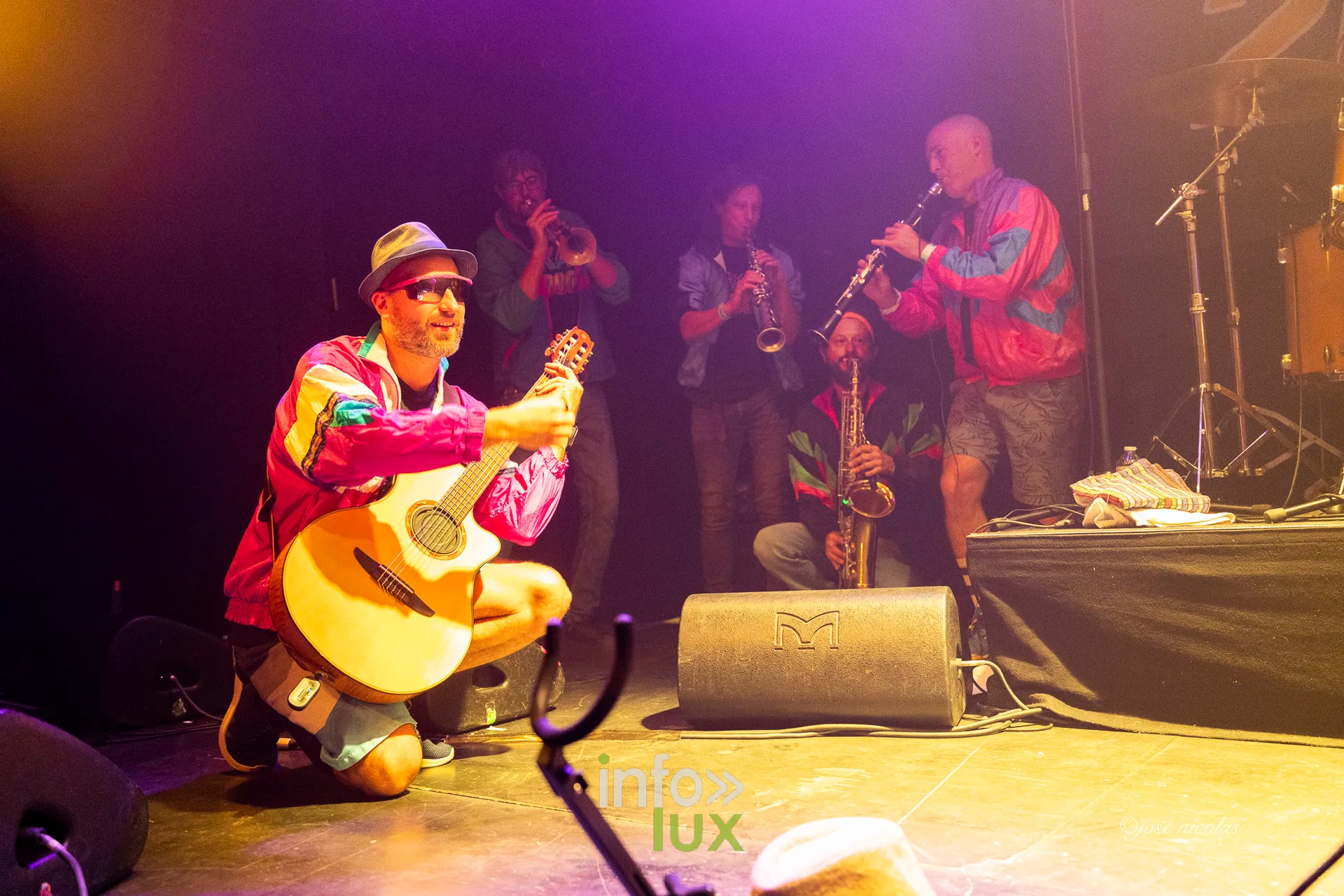 Le guitariste de SKA 2000 accroupi à la guitare acoustique, les cuivres derrière lui, L’Entrepôt d’Arlon, 25 septembre 2026