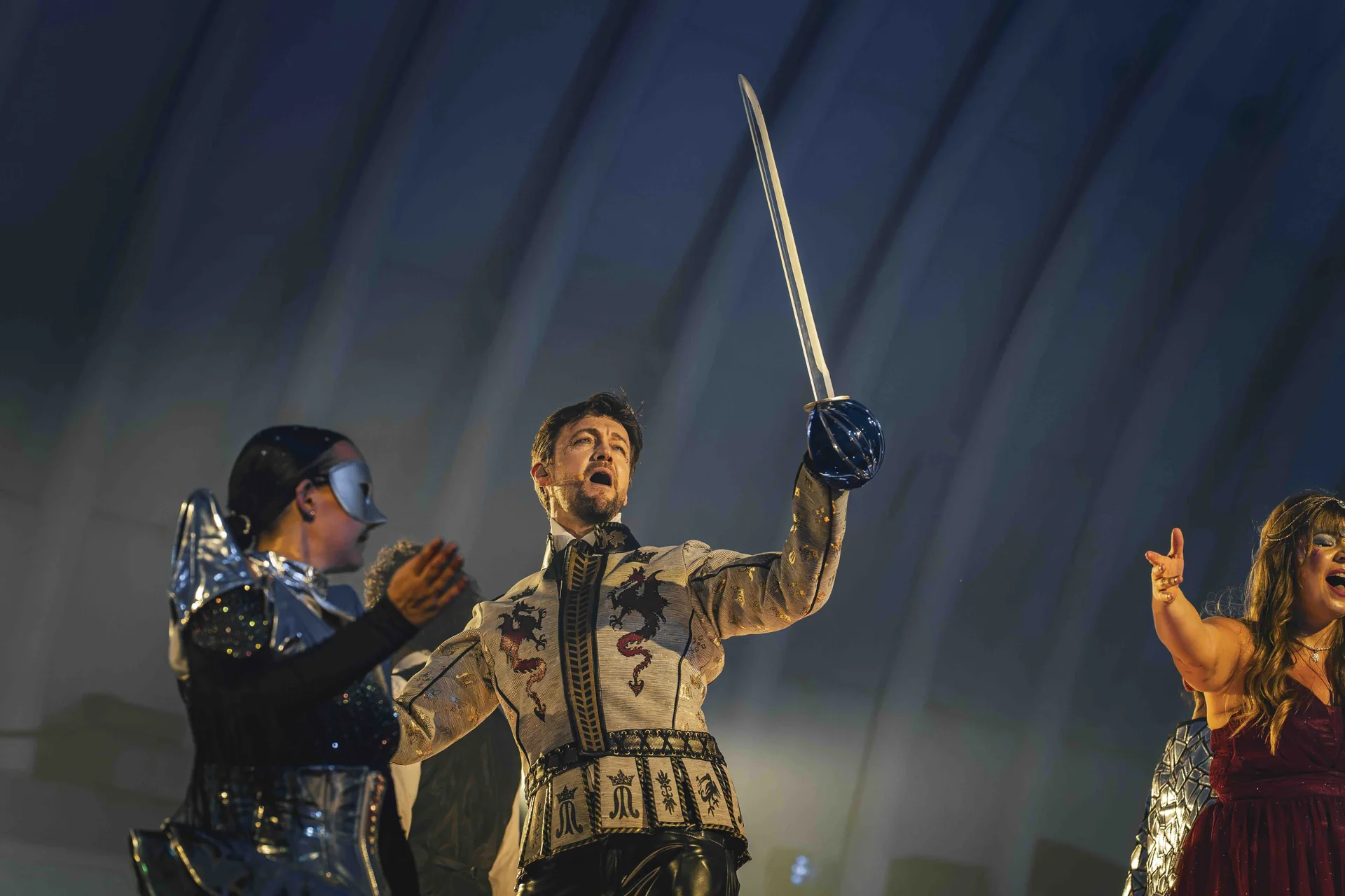 Le Comte de Monte-Cristal brandit le sabre en cristal du Val Saint-Lambert sur scène, entouré de deux comédiennes, spectacle de Luc Petit à Seraing