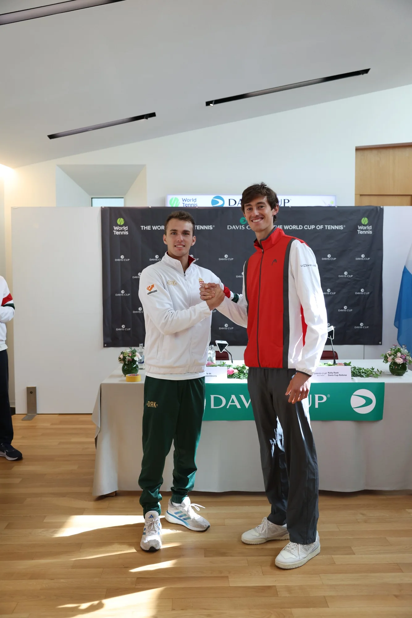 Un joueur luxembourgeois en rouge et un joueur hongrois en blanc posent devant le panneau Davis Cup