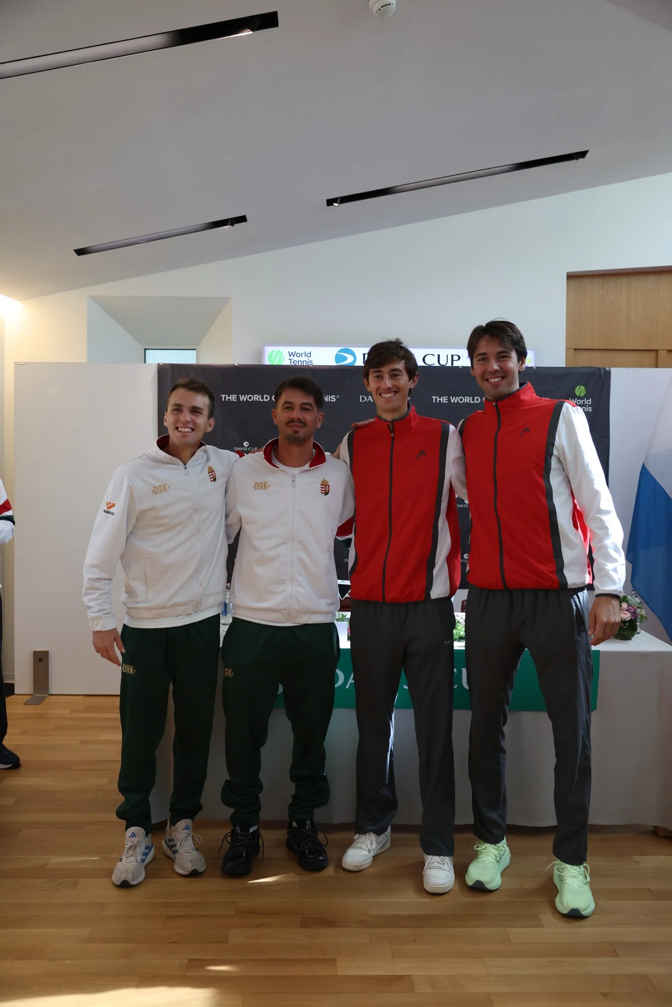 Deux joueurs luxembourgeois et deux joueurs hongrois posent ensemble devant le panneau Davis Cup