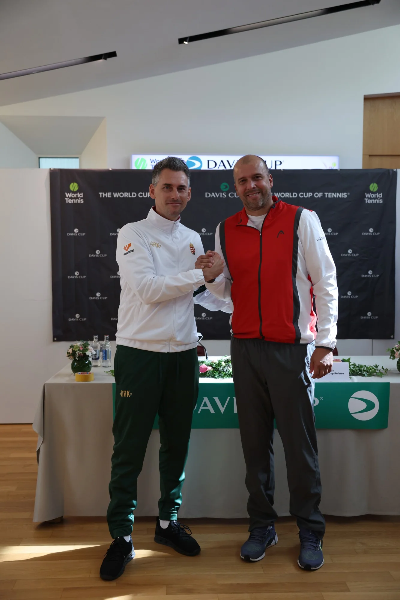 Un joueur luxembourgeois et un joueur hongrois se serrent la main devant le panneau Davis Cup